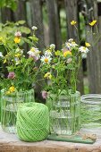 Vasendekoration mit grünem Garn und bunten Wiesenblumen
