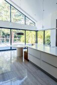 Island counter with integrated quarter-round bench at one end opposite glass wall with view of garden