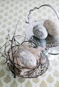 Eggs printed with patterns, lettering and characters in small Easter nest and on engraved silver plates