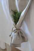 Bunch of rosemary in gathered end of ecru runner on white tablecloth