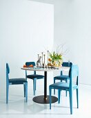 Essbereich mit rundem Tisch und pastellblauen, gepolsterten Metallstühlen, Tulpenstrauß und Hundefigur auf Tisch
