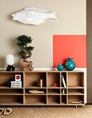Bonsai tree and Japanese ornaments on Scandinavian shelves below accent of colour on wall and paper fish sculpture