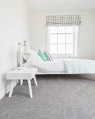 Weisses Bett und Nachtkästchen auf grauem Teppichboden