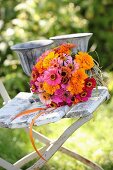 Colourful bouquet of zinnias and tagetes in glass vase on vintage garden chair