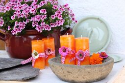 Orange candles decorated with flowers and ribbons in rustic bowl