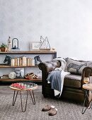 Vintage leather armchair, side table with chess board and shelf with books and decorative objects against a wall with patterned wallpaper