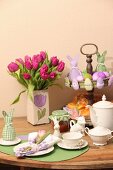 Easter place setting, vase of tulips and pastries and Easter ornaments on cake stand on wooden table