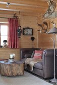 Sofa und rollbarer Baumstamm-Tisch in Zimmerecke einer Holzhütte