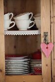 Cups and plates in cupboard with lace trim on shelves