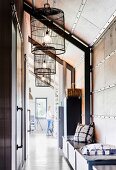 Chest with cushions and vintage cages as lampshades in a loft-like apartment