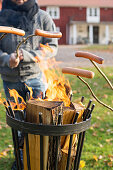 Grilling sausages on sticks over fire in brazier
