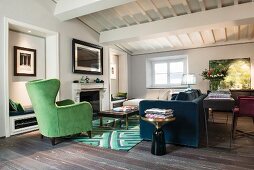 Green wing-back chair and blue sofa with console table against back in interior with white wood-beamed ceiling