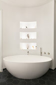 Oval free-standing bathtub against curved wall with niches