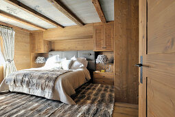 Fur rug and wood-clad walls in rustic bedroom