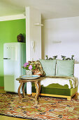 Grüne Sitzbank mit Tierfell und runder Tisch neben Raumteiler, Kühlschrank auf der anderen Seite