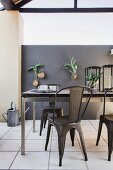 Esstisch mit Metallgestell und Metallstühle auf überdachter Terrasse, hängende Grünpflanzen an grauer Wand