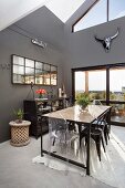 Long, industrial-style table and various chairs in high-ceilinged dining room with dark grey walls