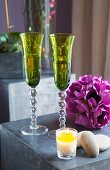 Elegant green Champagne flutes, purple artificial flower and lit tealight