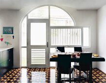 Essbereich mit schwarzen Stühlen und gedecktem Tisch vor Verglasung mit Rundbogen und Fenstertür, Fliesenboden mit geometrischem Retromuster