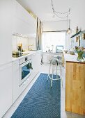 A compact kitchen with white fitted cupboards and a wooden breakfast bar