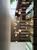 View from below up stairwell with illuminated spherical pendant lamps and glass balustrade panels