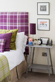 Grey bedside table next to bed with purple tartan headboard