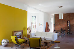 Gelbe Wand im offenen Wohnraum mit künstlerischem Möbelmix