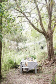 Laid garden table and chairs under pennant chain in the garden with tall trees