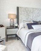 Nachttisch mit Lampe neben Doppelbett mit hohem Kopfteil in elegantem Schlafzimmer in Grautönen