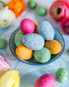 Colourful speckled eggs in bowl; Easter arrangement on pale blue tablecloth