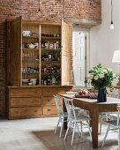 Rustic wooden cupboard with open doors and dining table in spacious kitchen with exposed brick wall