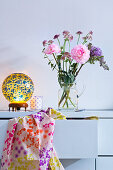 Flowers in glass jug and retro table lamp on chest of drawers