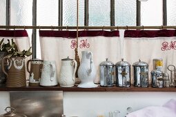 Arrangement of vintage objects on wall-mounted shelves against hand-made curtains embroidered with initials