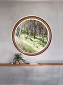 Round window with a view of the forest in a gray wall with a shelf