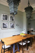 Antique lamps above dining table in front of artworks on panelled wall