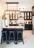Kitchen with black cupboards and bar stools next to counter with marble top