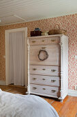 Old shabby-chic chest of drawers in bedroom with red-patterned wallpaper