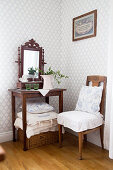 Chair with ruffled cushions next to small, antique table with mirror against classic wallpaper