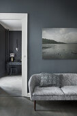 Retro sofa below gloomy landscape photograph on grey wall