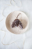 Three white-painted larch cones in clay dish with relief pattern