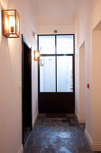 Slate-flagged floor, glass door and sconce lamps in hallway