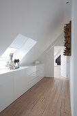 White high-gloss sideboard running along knee wall in corridor under sloping ceiling