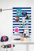 Striped pinboard above white desk and colourful accessories