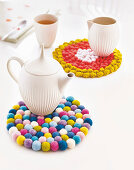A homemade pot holder made from colourful felt balls and crocheted dots