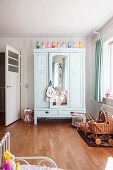 Mintgrüner Kleiderschrank mit Spiegeltür und Rattan-Puppenwagen im Mädchenzimmer
