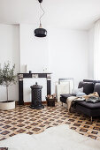 Cowhide rug on patterned tiled floor, grey sofa, wood-burning stove in front of disused fireplace and potted olive tree in living room