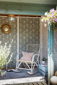 Old wooden rocking chair in summerhouse with patterned wallpaper on back wall