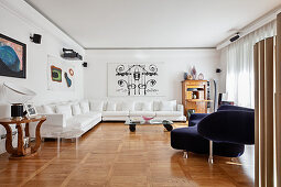 Weißes Ecksofa und blaues Designersofa in elegantem Wohnraum mit Kunstwerken and den Wänden