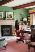 Log burner in fireplace and antique furniture in study with green walls