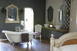 Free-standing bathtub in front of mirror on dark grey wall and washstand with concrete worksurface in ensuite bathroom